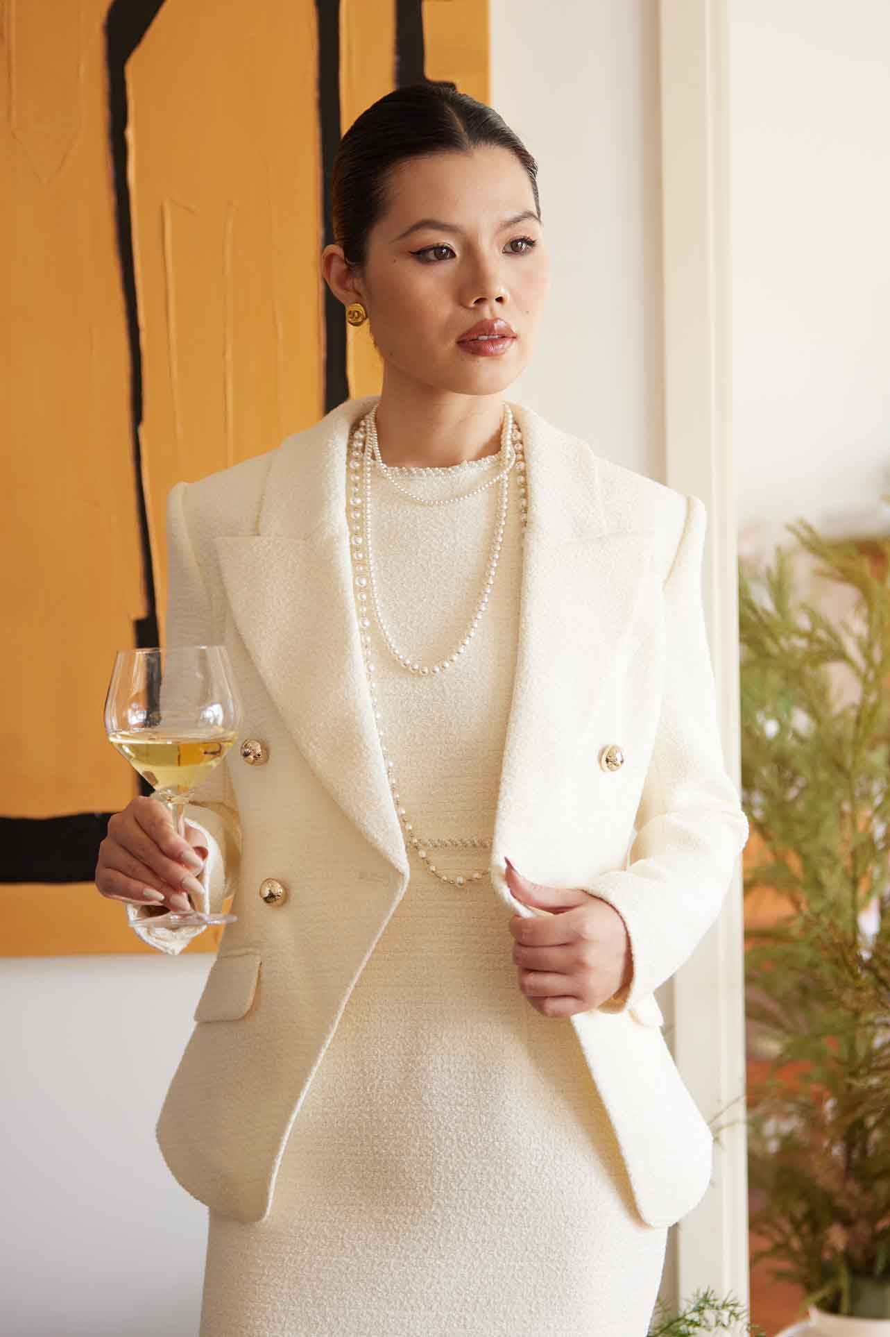 A professional woman wearing a sophisticated cream white double-breasted tweed blazer, featuring elegant gold buttons, a tailored slim fit, and classic flap pockets for a polished executive look.