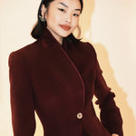 A professional woman wearing a sophisticated burgundy blazer suit with a classic shawl lapel and a white turtleneck, perfect for a high-end executive office look.