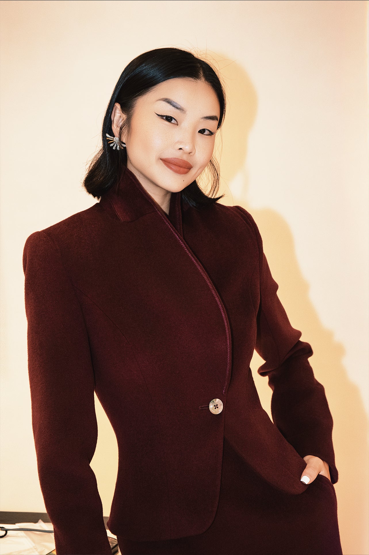 A professional woman wearing a sophisticated burgundy blazer suit with a classic shawl lapel and a white turtleneck, perfect for a high-end executive office look.
