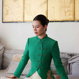 A professional woman wearing a stunning vibrant green blazer, featuring a traditional mandarin collar and elegant frog button detailing for a modern oriental-inspired executive look.