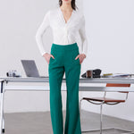 A professional woman wearing sophisticated emerald green high-waisted flare trousers, featuring a tailored slim fit through the hip and a stylish bootcut silhouette for an elegant office look.
