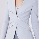 A professional woman wearing a sophisticated light grey tailored suit set, featuring a unique wrap-front blazer with criss-cross waist detailing and matching slim-fit trousers for a polished executive look.