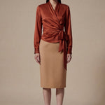 A professional woman wearing a high-end white silk wrap blouse with a side-tie detail, paired with a tailored black high-waisted pencil skirt for a sophisticated executive office look.