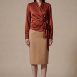 A professional woman wearing a high-end white silk wrap blouse with a side-tie detail, paired with a tailored black high-waisted pencil skirt for a sophisticated executive office look.