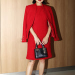 A professional woman wearing a sophisticated vibrant red tweed sleeveless mini dress, featuring a classic round neck, elegant frayed edges, and a slimming black waist belt for a chic holiday or office look.