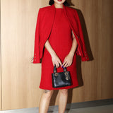 A professional woman wearing a sophisticated vibrant red tweed sleeveless mini dress, featuring a classic round neck, elegant frayed edges, and a slimming black waist belt for a chic holiday or office look.