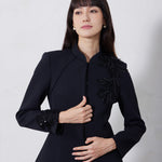 A professional woman wearing a sophisticated black skirt suit, featuring a mandarin collar with elegant leaf embroidery on the shoulder and skirt, and traditional frog button detailing for a modern oriental executive look.