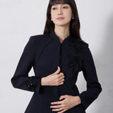 A professional woman wearing a sophisticated black skirt suit, featuring a mandarin collar with elegant leaf embroidery on the shoulder and skirt, and traditional frog button detailing for a modern oriental executive look.