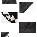 An elegant woman wearing a sophisticated black A-line midi dress, featuring exquisite white floral embroidery along the hem and professional three-quarter sleeves for a timeless formal look.