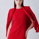 A professional woman wearing a sophisticated vibrant red tweed sleeveless mini dress, featuring a classic round neck, elegant frayed edges, and a slimming black waist belt for a chic holiday or office look.
