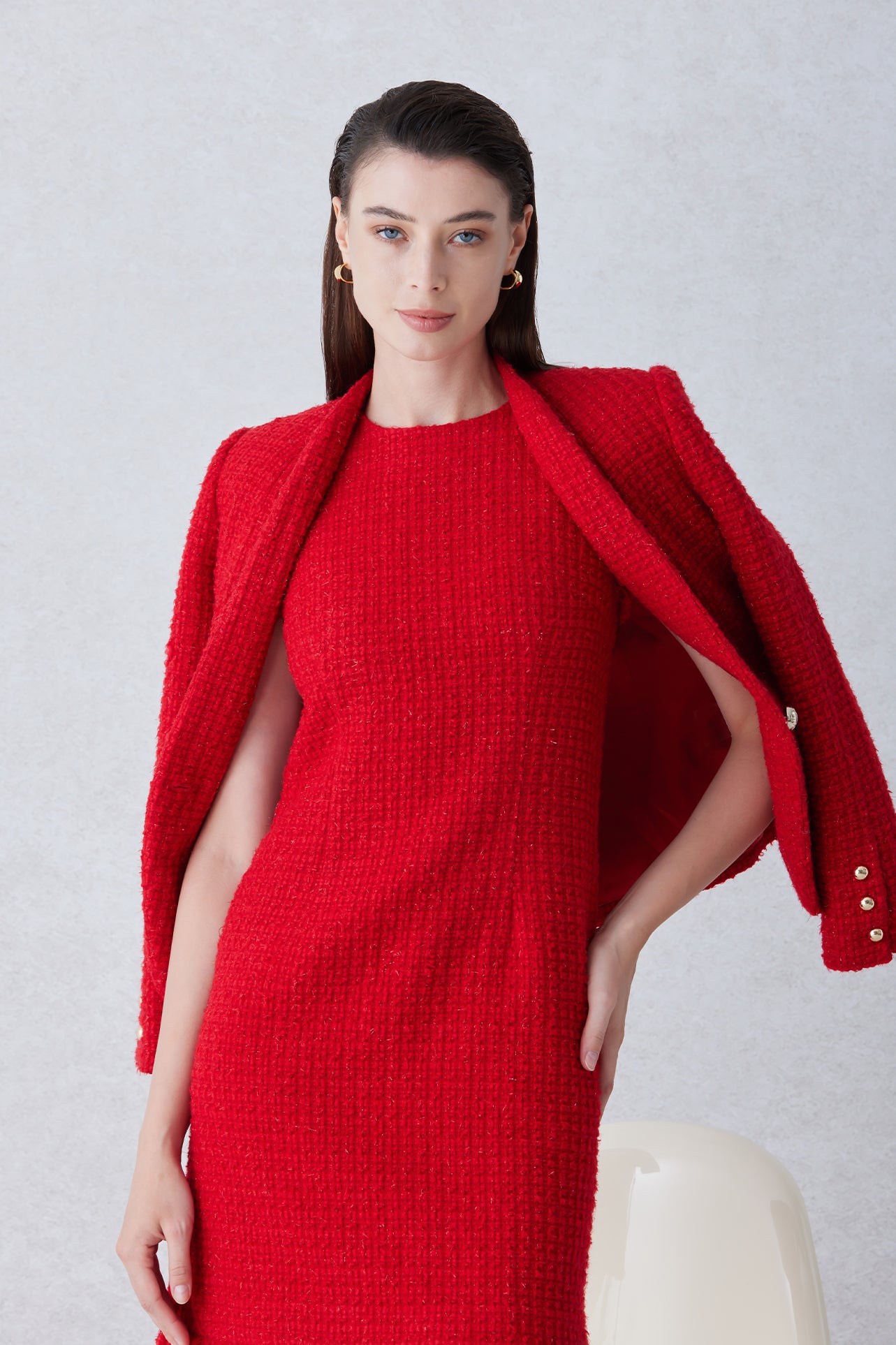 A professional woman wearing a sophisticated vibrant red tweed sleeveless mini dress, featuring a classic round neck, elegant frayed edges, and a slimming black waist belt for a chic holiday or office look.