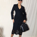 A professional woman wearing a sophisticated black long-sleeve coat dress, featuring an elegant tie-waist belt and notched lapels, styled over a white shirt for a polished executive business look.