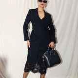 A professional woman wearing a sophisticated black long-sleeve coat dress, featuring an elegant tie-waist belt and notched lapels, styled over a white shirt for a polished executive business look.