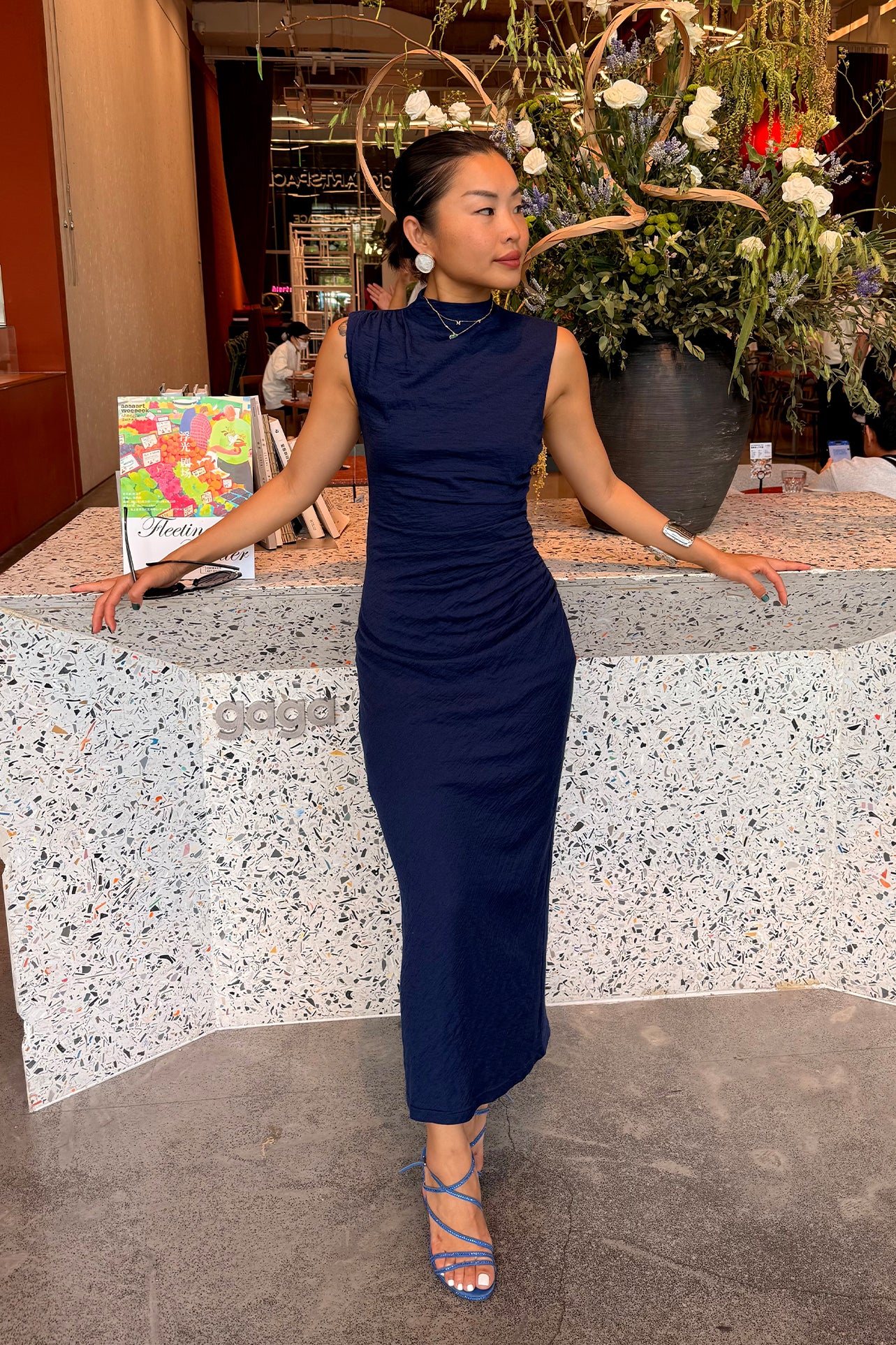 A professional woman wearing a sophisticated navy blue sleeveless midi dress, featuring an elegant high neckline and flattering ruched detailing along the side for a slim-fit executive look.