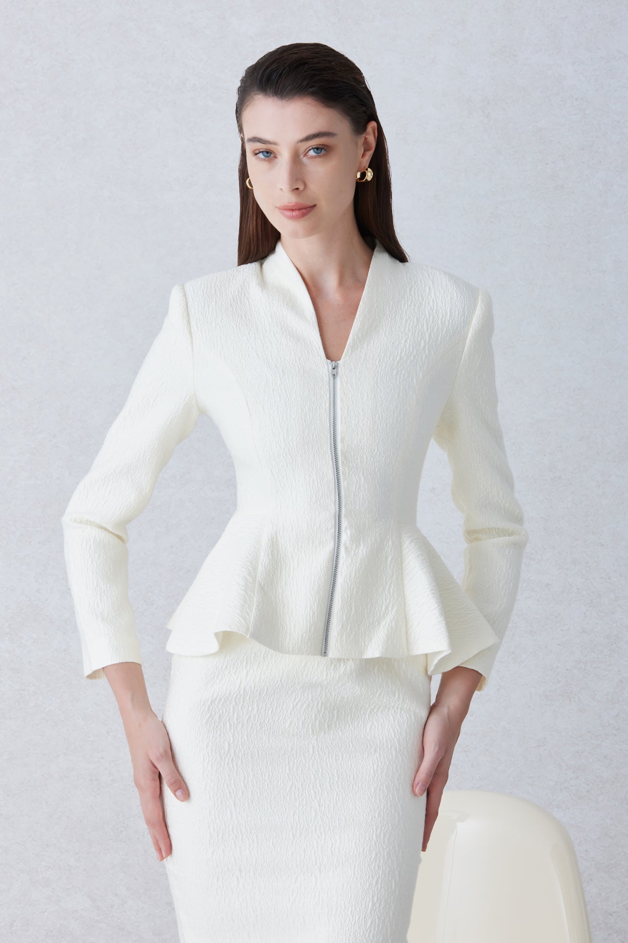 A professional woman wearing a sophisticated cream tweed skirt suit, featuring a tailored jacket with a modern front zipper and an elegant stand collar for a polished executive office look.