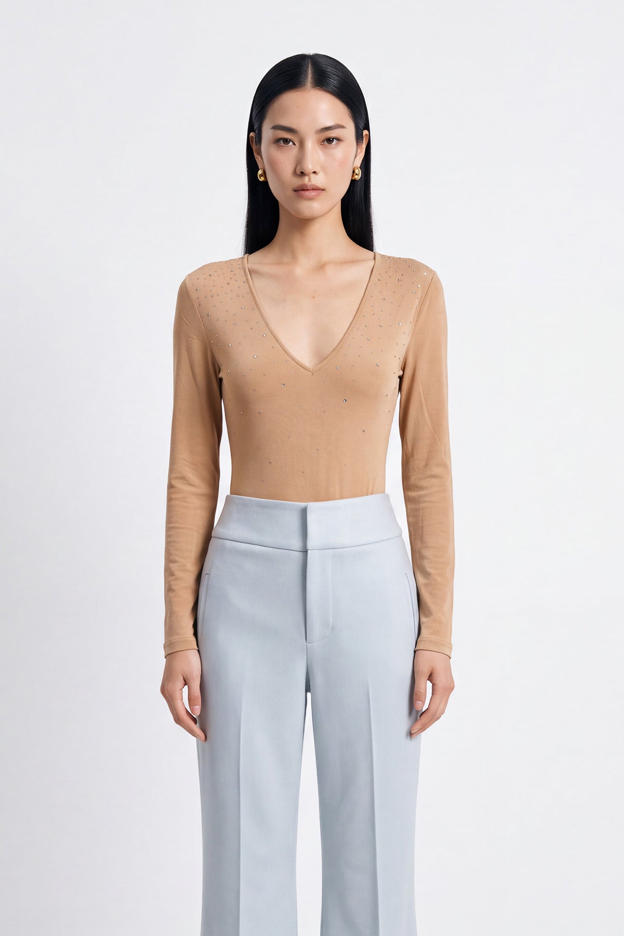 A style comparison of two elegant women's long-sleeve deep V-neck tops featuring subtle rhinestone crystal embellishments; shown on the left in nude camel tucked into tailored trousers, and on the right in pale mint green styled with a white skirt.