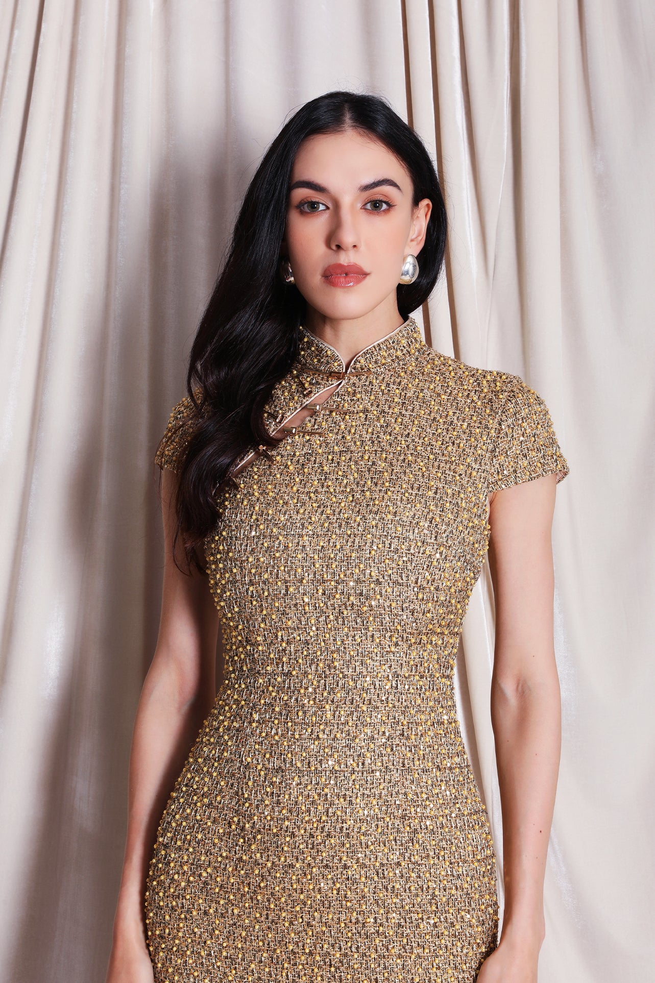 A professional woman wearing a stunning luxurious gold sequined modern qipao dress, featuring a traditional mandarin collar, short cap sleeves, and a slim-fit floor-length silhouette for a formal evening gala.