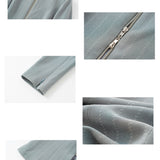 A professional woman wearing a sophisticated grey pinstripe zip-up blazer, featuring a thin white belt with a gold buckle and a tailored slim fit for a modern office look.