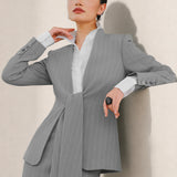A beautiful professional model wearing an elegant grey pinstripe collarless blazer featuring a distinctive tie-front knot at the waist, styled with a crisp white collared shirt underneath for a modern corporate chic look.