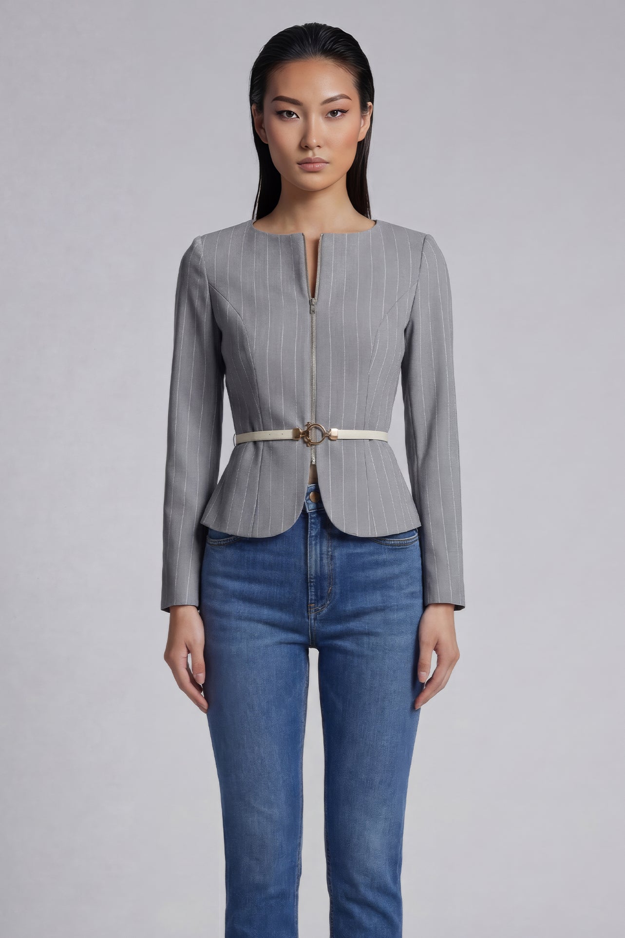 A professional woman wearing a sophisticated grey pinstripe zip-up blazer, featuring a thin white belt with a gold buckle and a tailored slim fit for a modern office look.