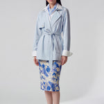 A professional woman wearing an elegant light blue short trench coat with a waist-tie belt and white sleeve cuffs, perfect for a smart casual spring office look.