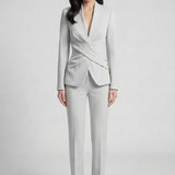 A professional woman wearing a sophisticated light grey tailored suit set, featuring a unique wrap-front blazer with criss-cross waist detailing and matching slim-fit trousers for a polished executive look.