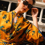 A beautiful woman modeling an elegant mustard yellow modern Chinese jacket, featuring intricate blue phoenix embroidery, a sophisticated mandarin collar, and wide kimono sleeves with a matching waist tie