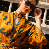 A beautiful woman modeling an elegant mustard yellow modern Chinese jacket, featuring intricate blue phoenix embroidery, a sophisticated mandarin collar, and wide kimono sleeves with a matching waist tie