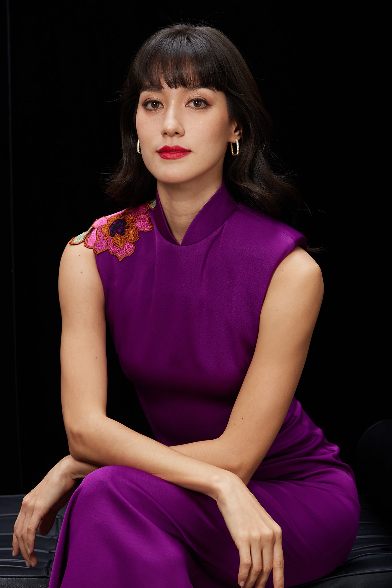 A professional woman wearing a stunning purple satin sleeveless dress, featuring a traditional mandarin collar and delicate floral embroidery on the shoulder for a modern oriental-inspired formal look.