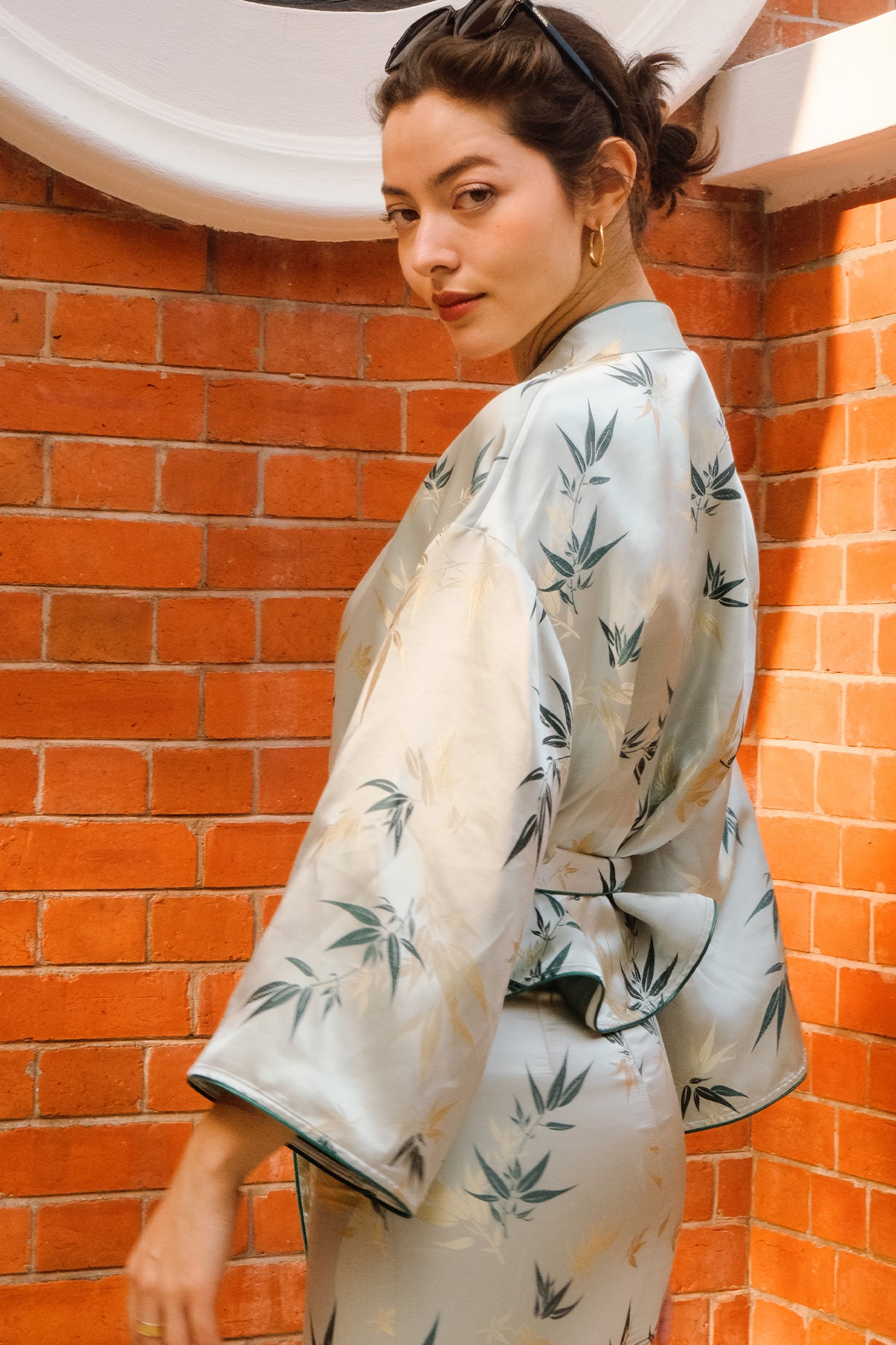 A professional woman modeling an elegant light sage green silk wrap jacket, featuring dark green bamboo leaf prints, a sophisticated mandarin collar with keyhole detail, and wide kimono sleeves.