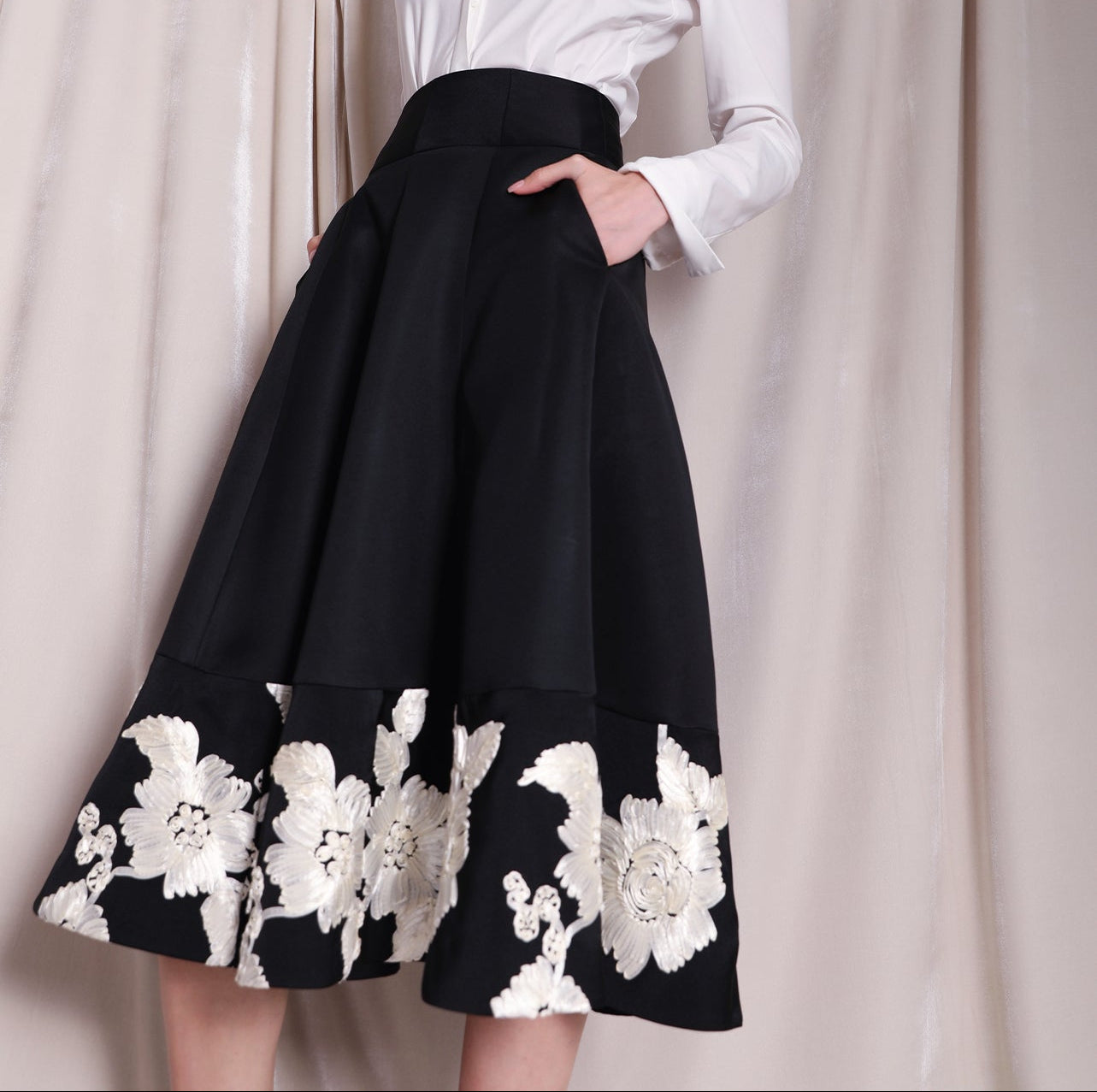 An elegant woman wearing a sophisticated black A-line midi dress, featuring exquisite white floral embroidery along the hem and professional three-quarter sleeves for a timeless formal look.