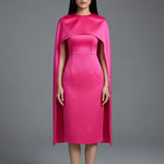 Two professional women wearing sophisticated cape-style dresses: one in a classic black and white monochrome with a thin belt, and the other in a vibrant magenta pink, perfect for a powerful and elegant evening look.