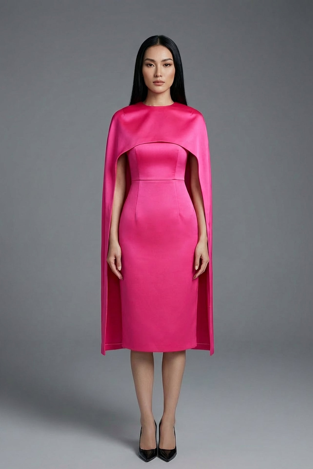 Two professional women wearing sophisticated cape-style dresses: one in a classic black and white monochrome with a thin belt, and the other in a vibrant magenta pink, perfect for a powerful and elegant evening look.