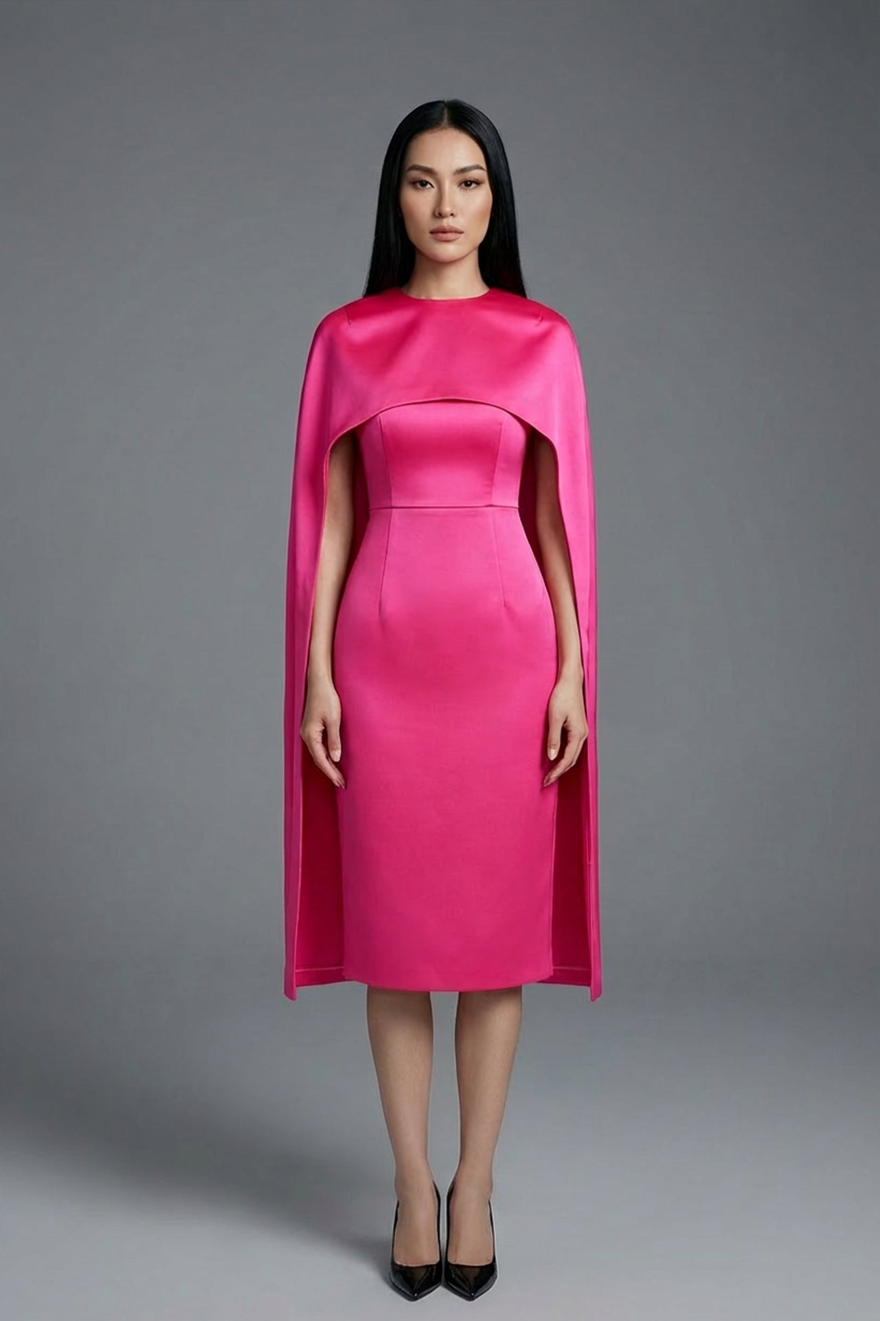 Two professional women wearing sophisticated cape-style dresses: one in a classic black and white monochrome with a thin belt, and the other in a vibrant magenta pink, perfect for a powerful and elegant evening look.