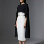 Two professional women wearing sophisticated cape-style dresses: one in a classic black and white monochrome with a thin belt, and the other in a vibrant magenta pink, perfect for a powerful and elegant evening look.