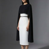 Two professional women wearing sophisticated cape-style dresses: one in a classic black and white monochrome with a thin belt, and the other in a vibrant magenta pink, perfect for a powerful and elegant evening look.