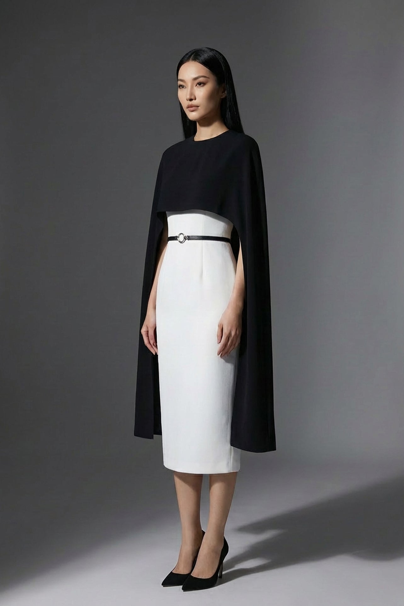 Two professional women wearing sophisticated cape-style dresses: one in a classic black and white monochrome with a thin belt, and the other in a vibrant magenta pink, perfect for a powerful and elegant evening look.