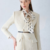 A professional woman wearing a sophisticated cream white tweed skirt suit, featuring a double-breasted blazer with gold buttons, a slim black belt, and an elegant polka dot pussy bow tie for a polished French chic office look.