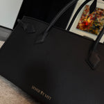 A sophisticated plum purple tote bag crafted from premium pebbled leather, displayed next to a matching shade of luxury lipstick, representing an elegant executive fashion set.