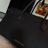 A sophisticated plum purple tote bag crafted from premium pebbled leather, displayed next to a matching shade of luxury lipstick, representing an elegant executive fashion set.