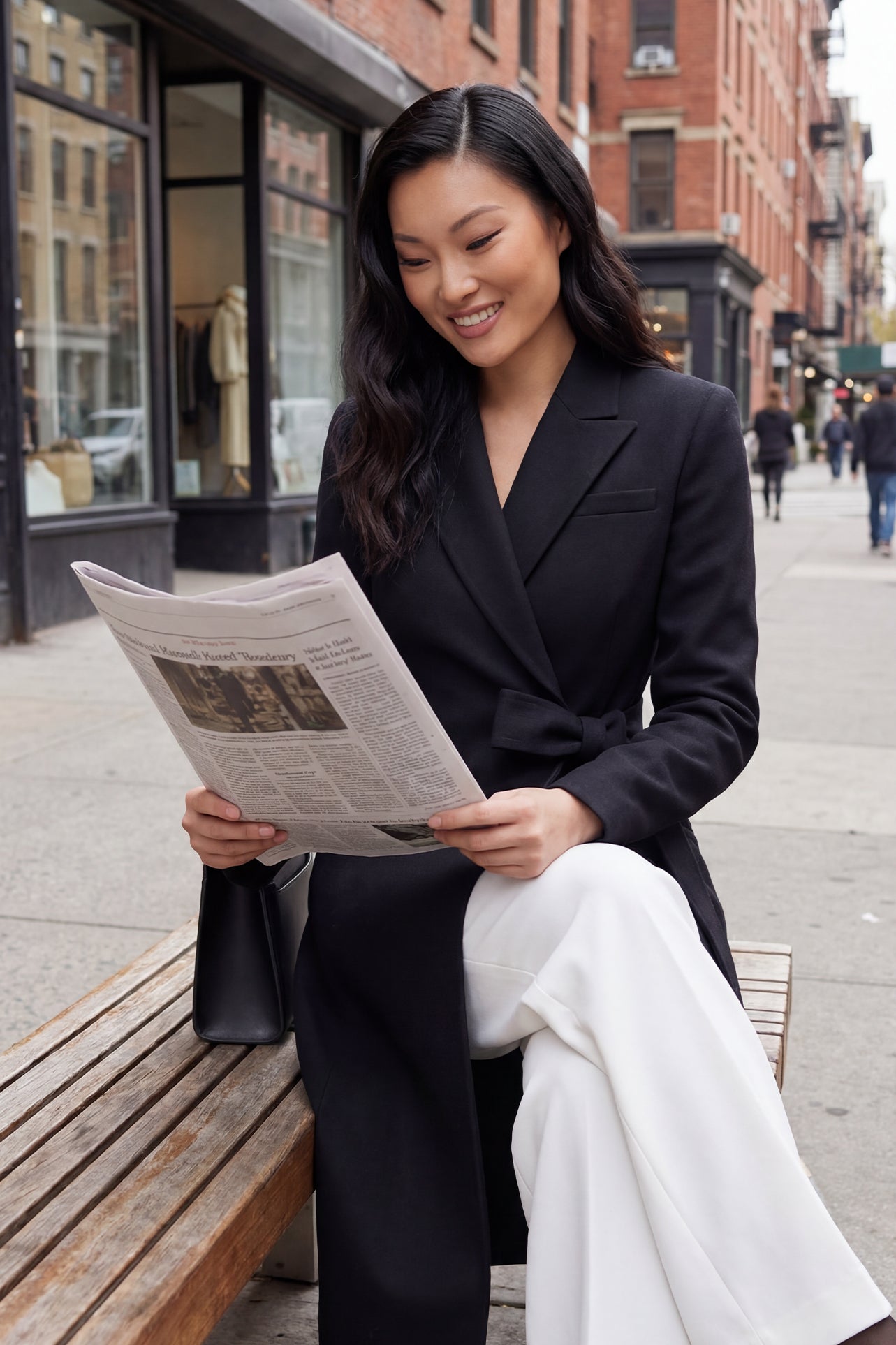 A professional woman wearing a sophisticated black long-sleeve coat dress, featuring an elegant tie-waist belt and notched lapels, styled over a white shirt for a polished executive business look.