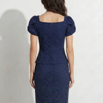 A professional woman modeling an elegant navy blue lace short top, featuring a retro square neckline, romantic short puff sleeves, and a series of pearl and rhinestone frog closures on the front with a tailored triangular split hem, paired with light blue high-waisted jeans.