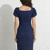 A professional woman modeling an elegant navy blue lace short top, featuring a retro square neckline, romantic short puff sleeves, and a series of pearl and rhinestone frog closures on the front with a tailored triangular split hem, paired with light blue high-waisted jeans.