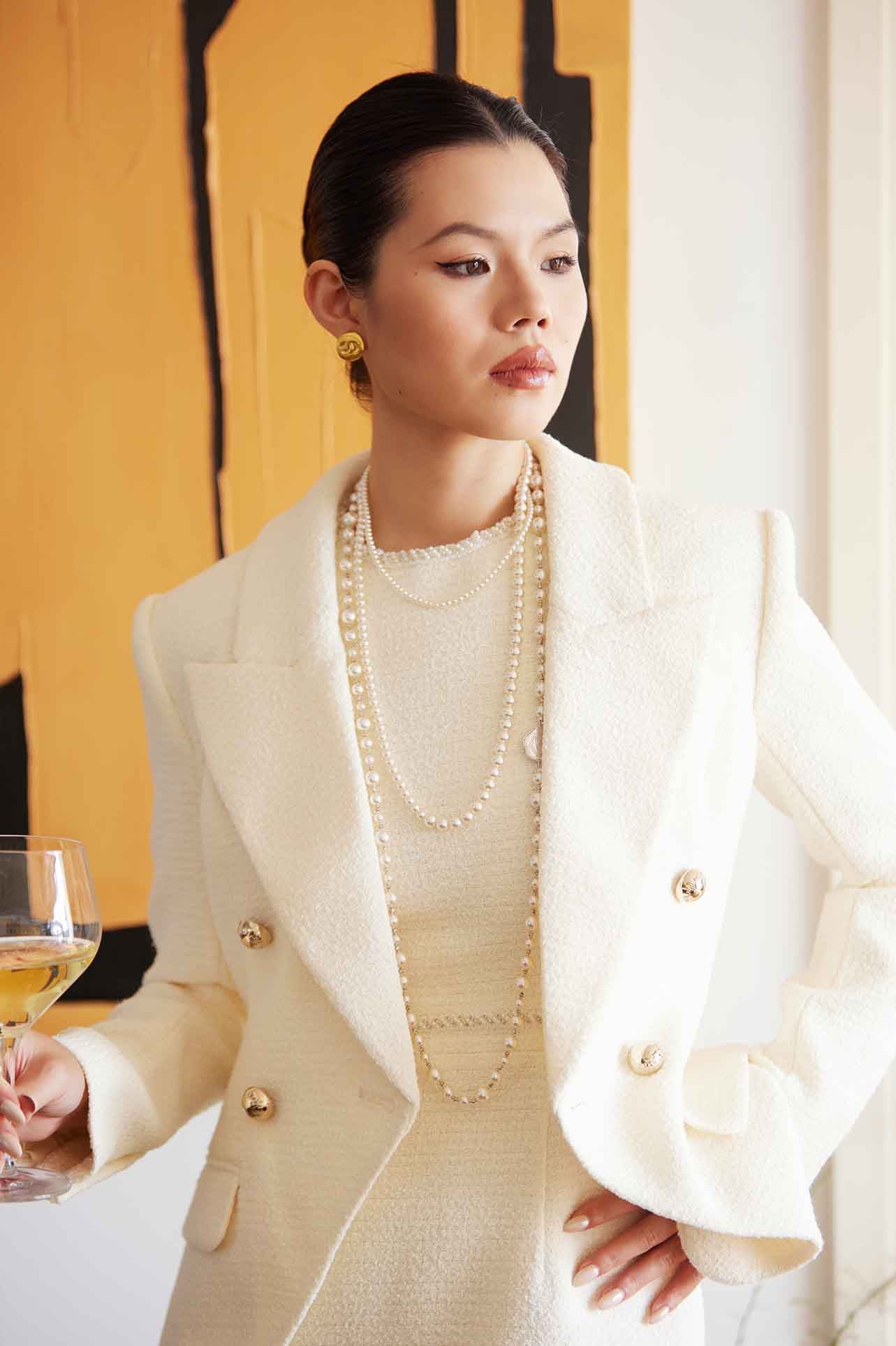 A professional woman wearing a sophisticated cream white double-breasted tweed blazer, featuring elegant gold buttons, a tailored slim fit, and classic flap pockets for a polished executive look.