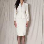 A professional woman wearing a sophisticated cream tweed skirt suit, featuring a tailored jacket with a modern front zipper and an elegant stand collar for a polished executive office look.