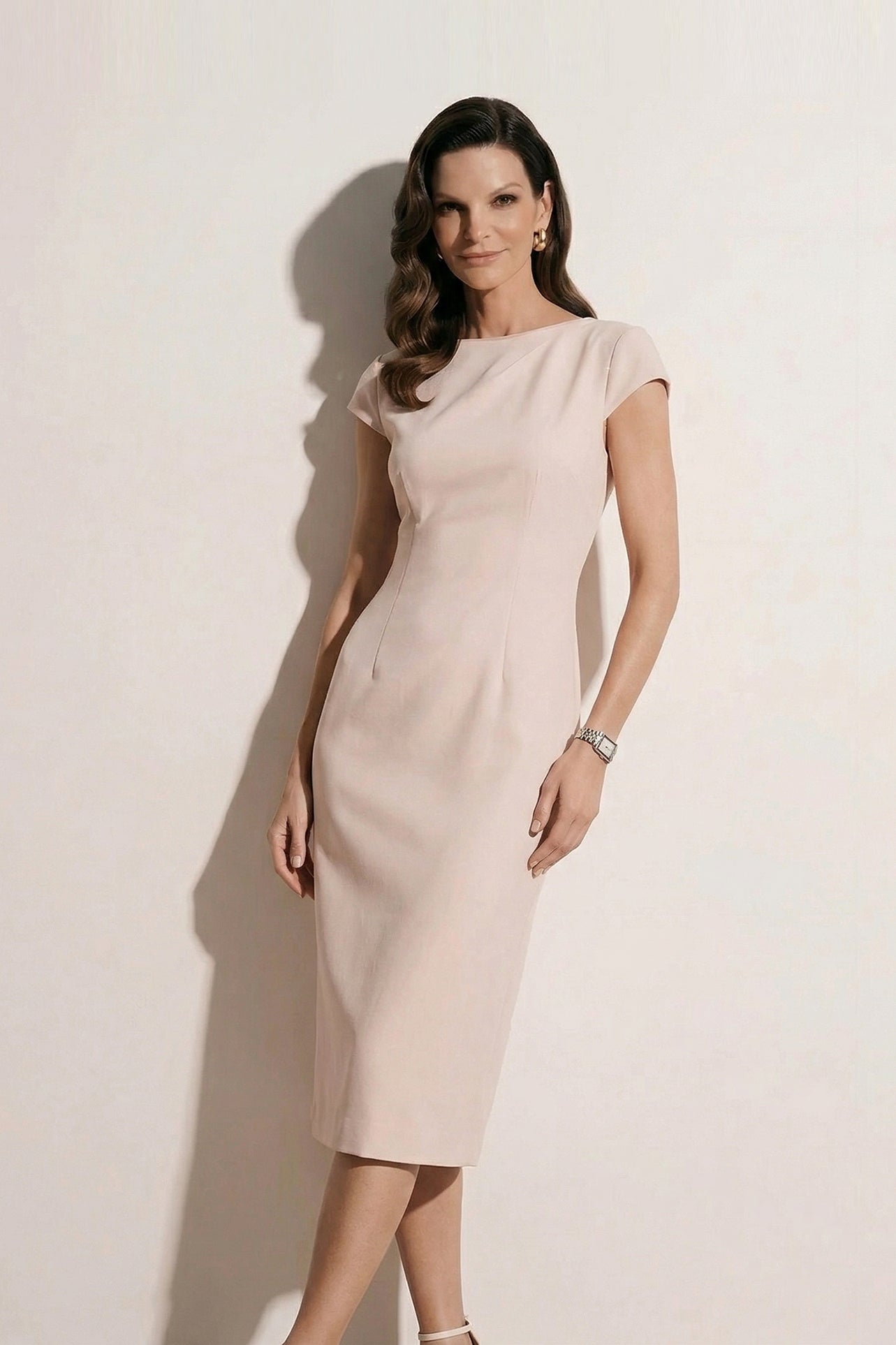 A professional woman modeling an elegant pale pink sheath dress, featuring a sophisticated crew neckline, cap sleeves, and a tailored slim fit with princess seams for a timeless executive look.