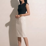 A professional woman modeling an elegant black and white color-block sheath dress, featuring a sleeveless black bodice with metallic hardware and a tailored white pencil skirt for a sophisticated executive look.