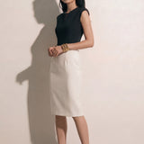 A professional woman modeling an elegant black and white color-block sheath dress, featuring a sleeveless black bodice with metallic hardware and a tailored white pencil skirt for a sophisticated executive look.