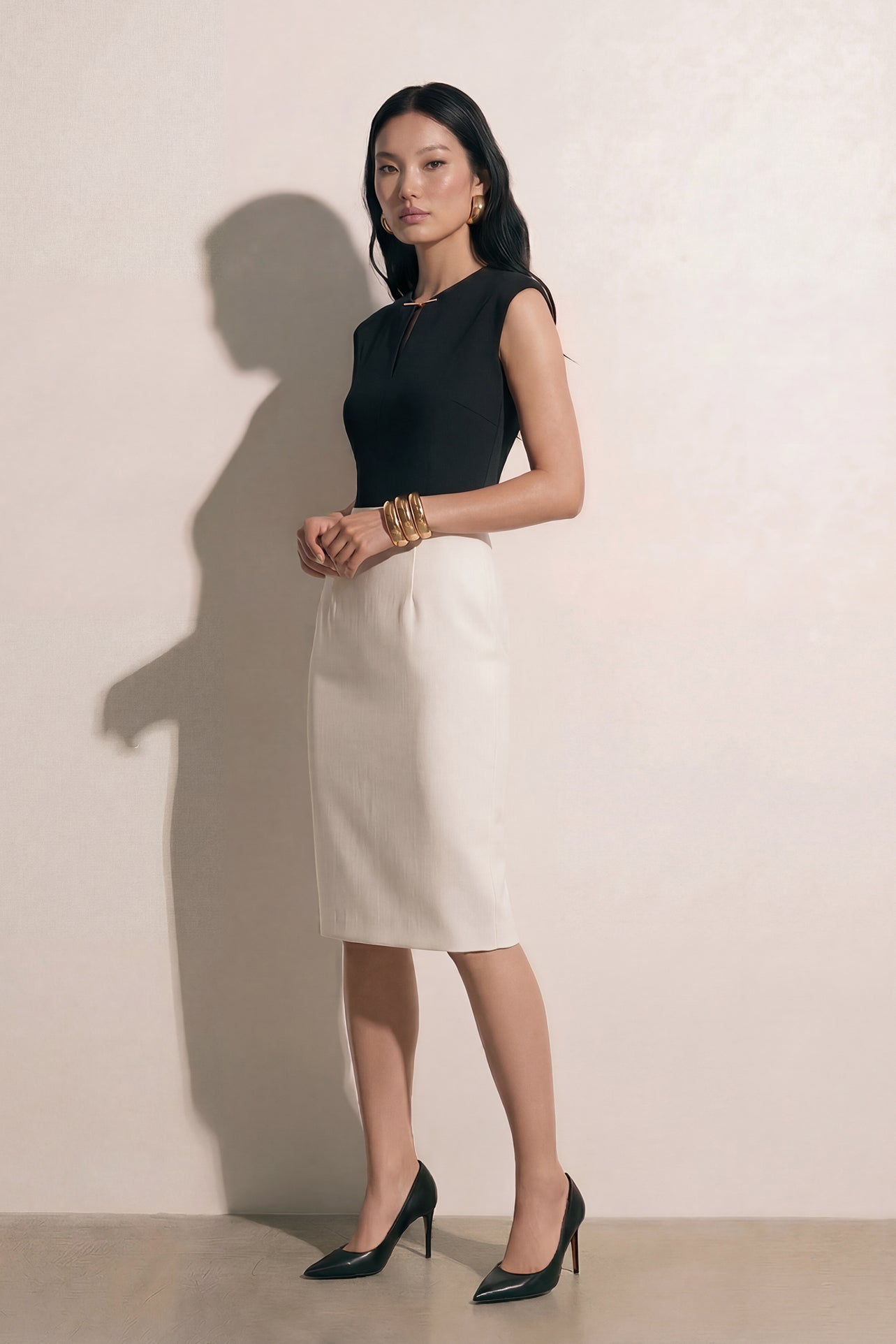 A professional woman modeling an elegant black and white color-block sheath dress, featuring a sleeveless black bodice with metallic hardware and a tailored white pencil skirt for a sophisticated executive look.
