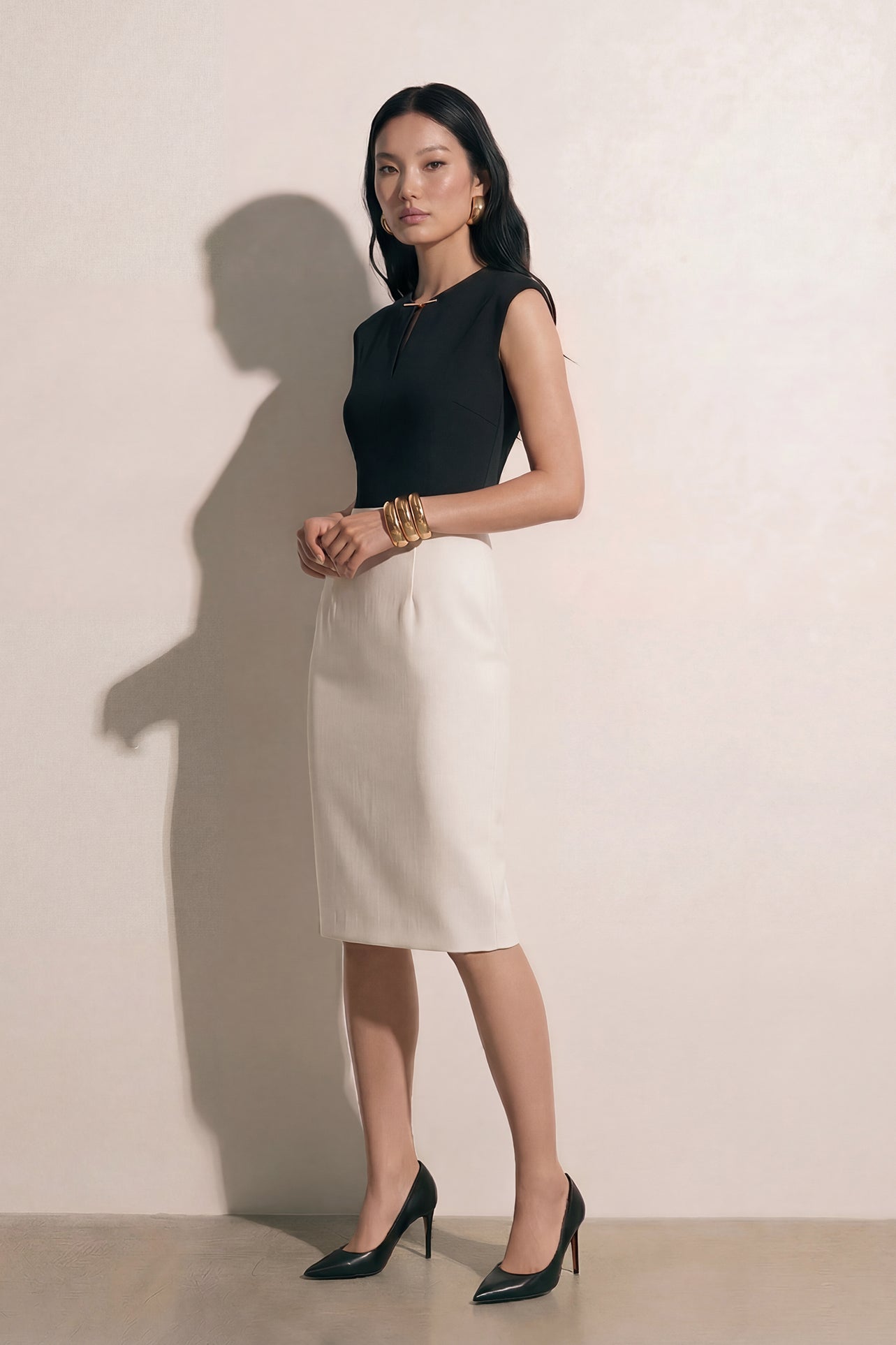 A professional woman modeling an elegant black and white color-block sheath dress, featuring a sleeveless black bodice with metallic hardware and a tailored white pencil skirt for a sophisticated executive look.